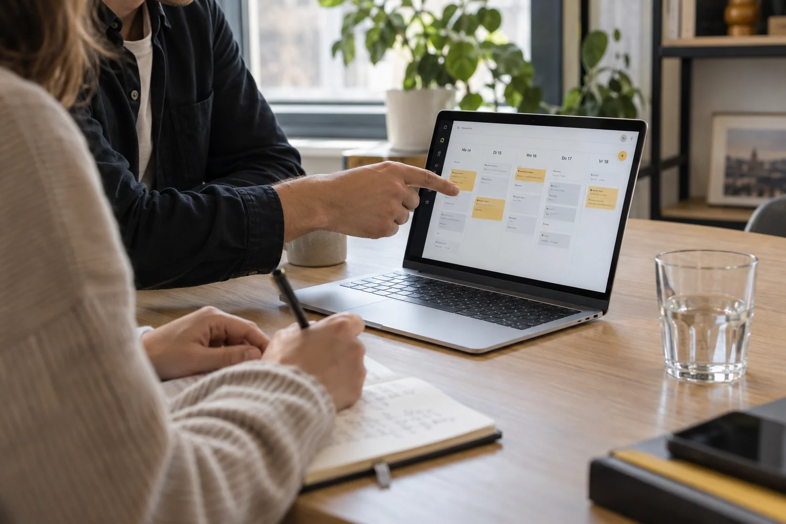 Twee professionals bespreken een planning op een laptop aan een houten vergadertafel